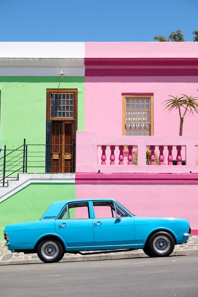 blue sedan parked beside pink and green house