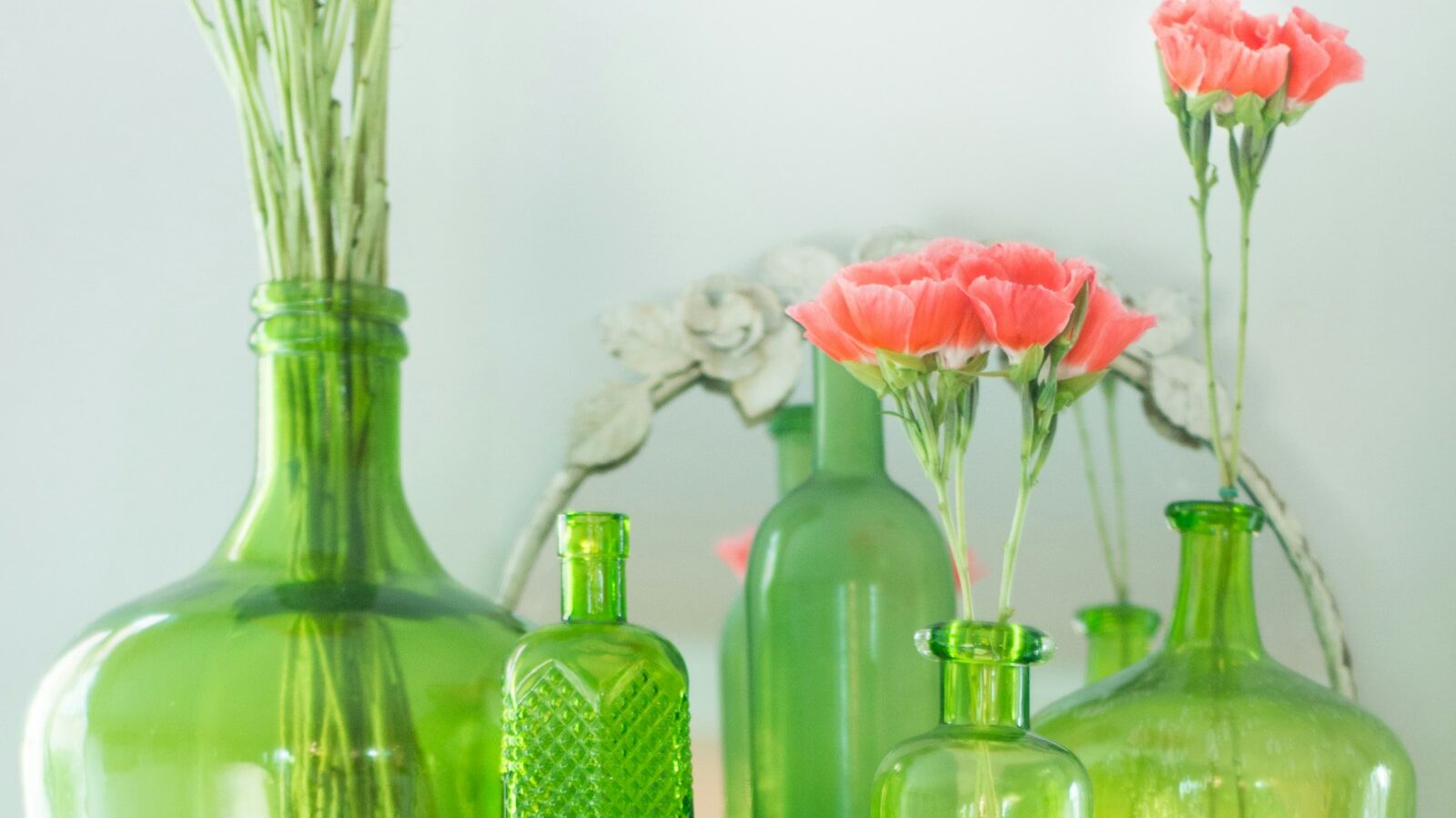 green grass bottles with pink flowers beside white wall